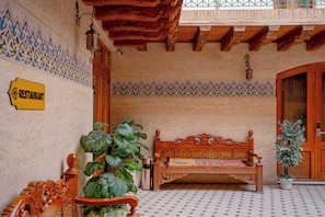 A traditional interior with a wooden bench, a sign indicating a restaurant, and a tiled floor. - Asal Boutique Hotel (Bukhara)