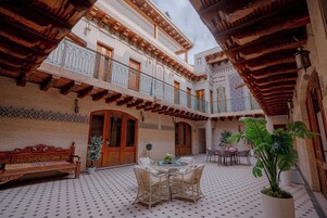 A courtyard with a bench, wicker furniture, potted plants, and a tiled floor.