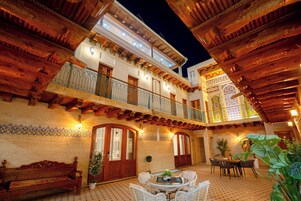 A courtyard with a wooden bench, a round table with chairs, and a balcony with railings.