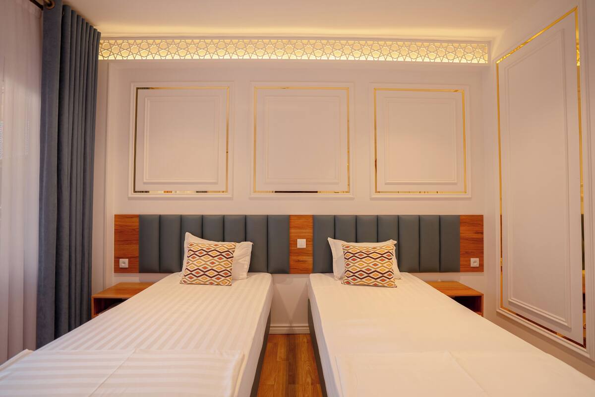 Quarto de hotel com duas camas, cabeceira de madeira e luminária decorativa no teto.