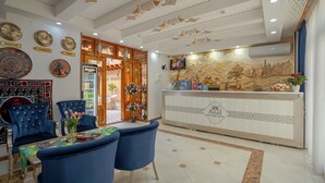 A hotel lobby with a reception desk, blue chairs, a dining area, decorative plates, and a television screen. - Asal Boutique Hotel (Bukhara)