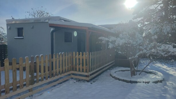 A small, single-story building with a porch, a wooden fence, and a snow-covered landscape. - Vu's Home - Apartment Deluxe 50m2 (Prague)