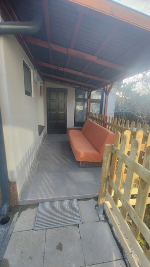 A covered outdoor area with a wooden bench, a door, and a window.