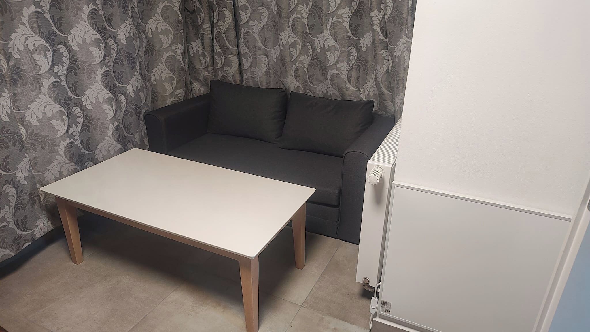 A room with a white table, a dark sofa, and a white radiator.