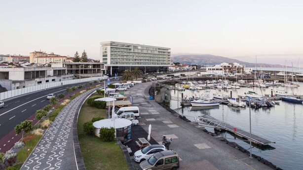 A marina with boats docked, a road with cars, and a modern building with a flat roof. - Atlantic City - Marina (Ponta Delgada)
