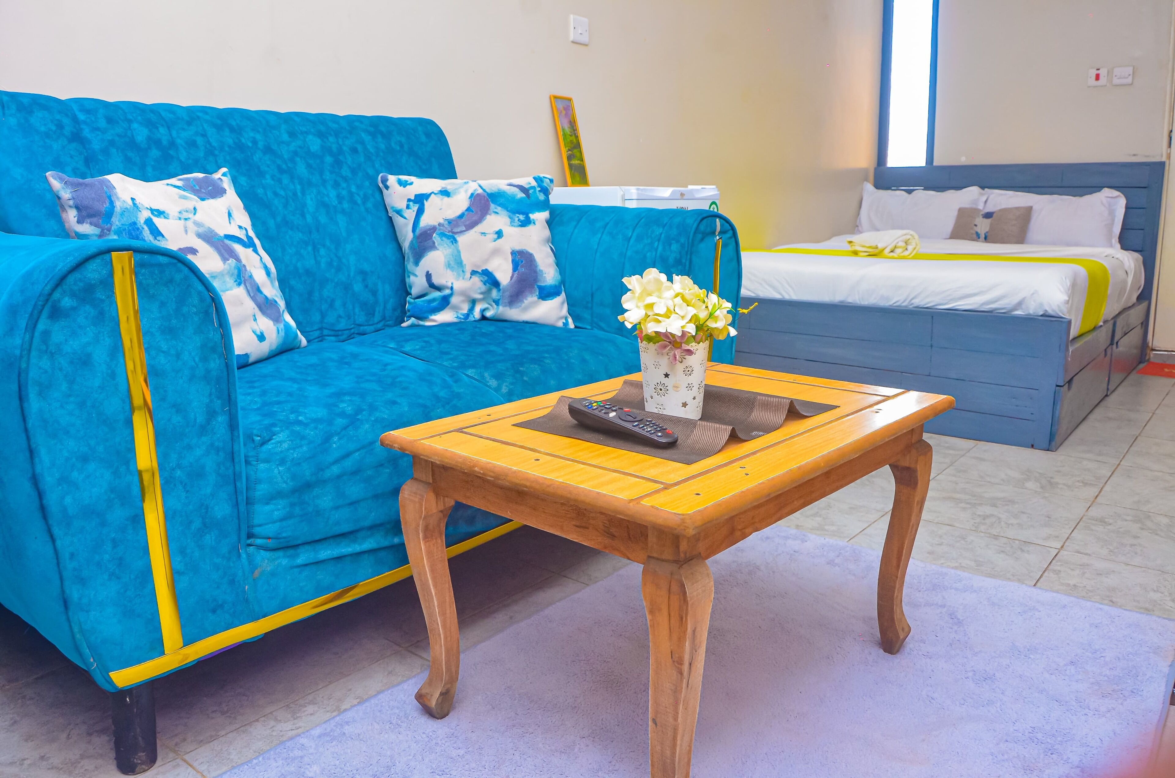 Een kamer met een blauwe bank, een houten tafel met een bloevas en een bed met wit beddengoed.