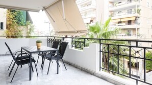 Un balcón con una mesa y sillas, una planta en maceta y vistas a edificios cercanos.