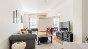 Uma sala de estar moderna com um sofá cinzento, uma mesa de centro e uma televisão em um suporte preto.