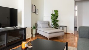Uma sala de estar moderna com televisão de tela plana, um sofá cinza, uma mesa de centro e um vaso de planta.