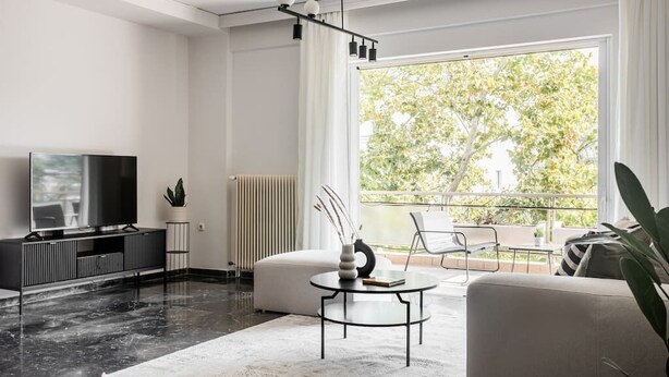 Un salon moderne doté d’une grande fenêtre, d’un téléviseur à écran plat, d’un canapé, d’une table basse et d’un radiateur.