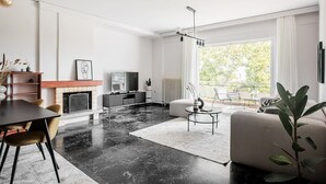 Un salon moderne doté d’une cheminée, d’un coin repas et d’une grande fenêtre offrant une vue sur la verdure environnante.