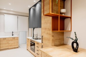 Modern kitchen with light and dark wood cabinetry, oven, and a wooden shelf unit.