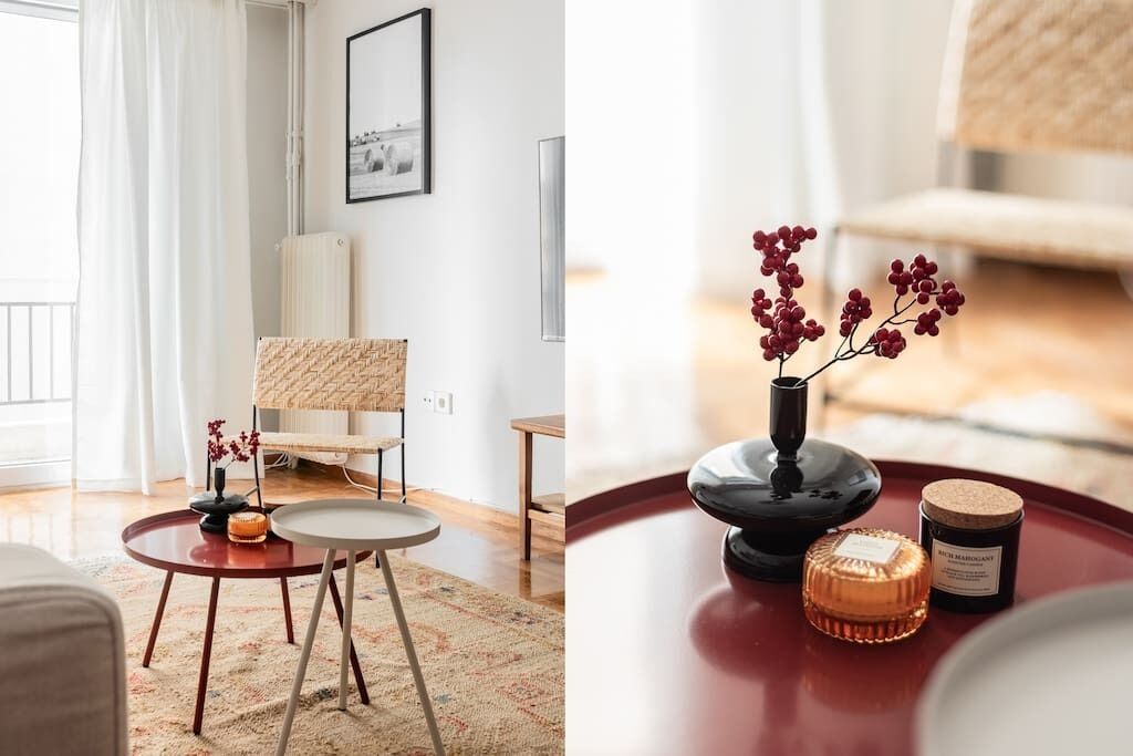 A modern living room with a round coffee table, a wicker chair, and a vase with red berries.