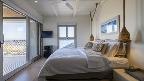 A bedroom with a large bed, a ceiling fan, a TV, and a view through a sliding glass door. - Luxurious villa in Paros island. Walking to the beach. Close to Naoussa Town.  (Ιστέρνι)