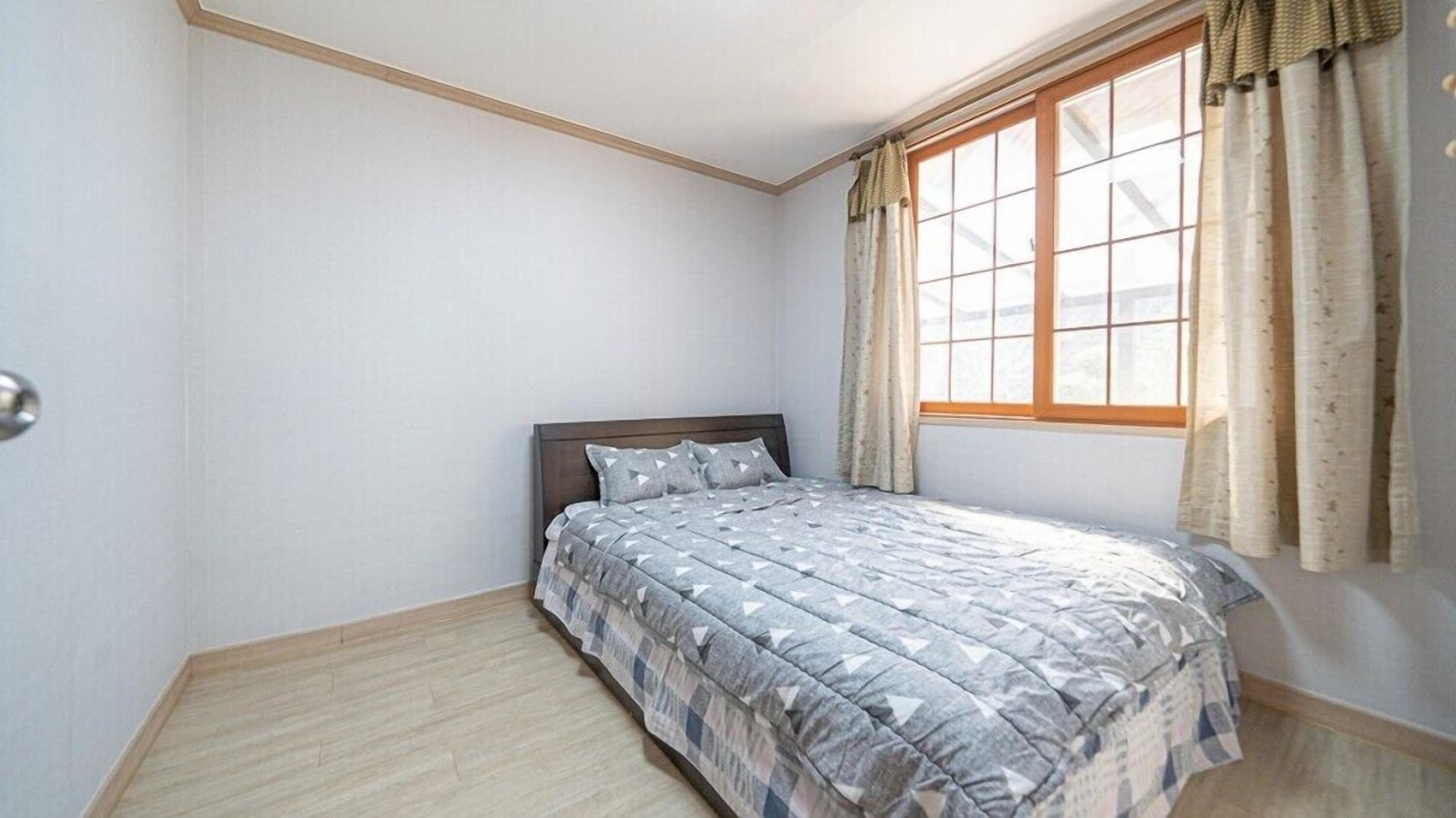 Un dormitorio con cama, ventana con cortinas y suelo de madera.