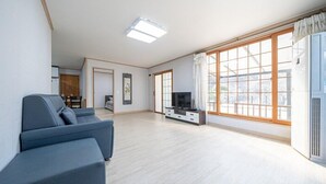 Un salón amplio con un ventanal grande, un sofá, un televisor y una puerta corredera que da a otra habitación.