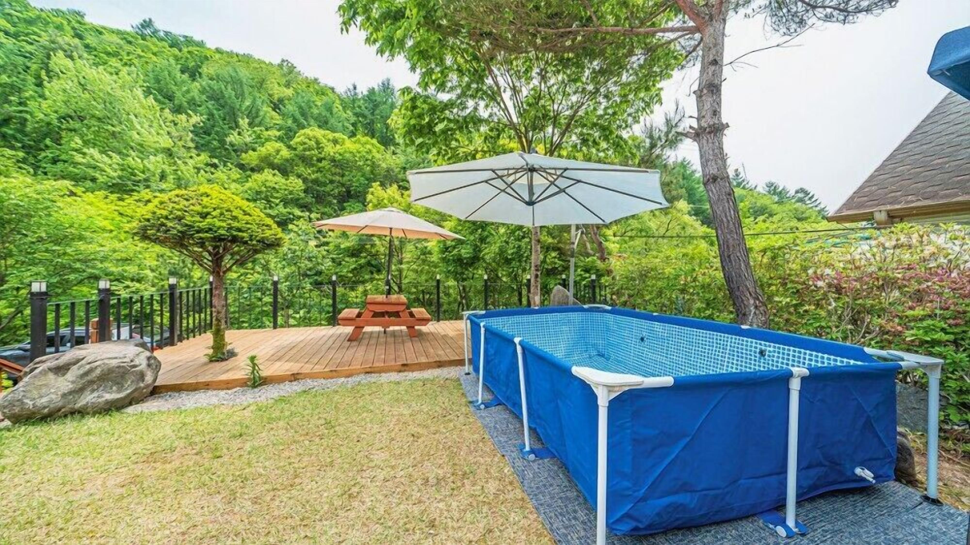 Ein Freibad mit Holzterrasse, Picknicktisch und Sonnenschirmen.