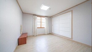 Una habitación con piso de madera, un banco, una ventana con cortinas y una puerta corredera.
