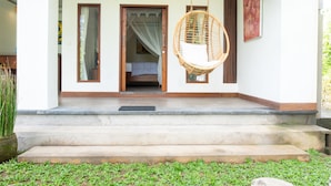 A porch with a hanging chair, a door leading to a room, and a small step.