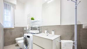Casa de banho moderna com máquina de lavar, sanita, lavatório e porta-toalhas.