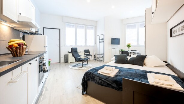 Quarto de hotel moderno com cama, escrivaninha, cadeira, televisão e cozinha equipada, com frutas.