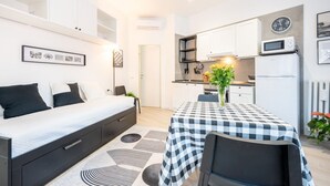 Quarto compacto com cama, mesa de cabeceira e uma mesa de jantar coberta por um tecido xadrez.
