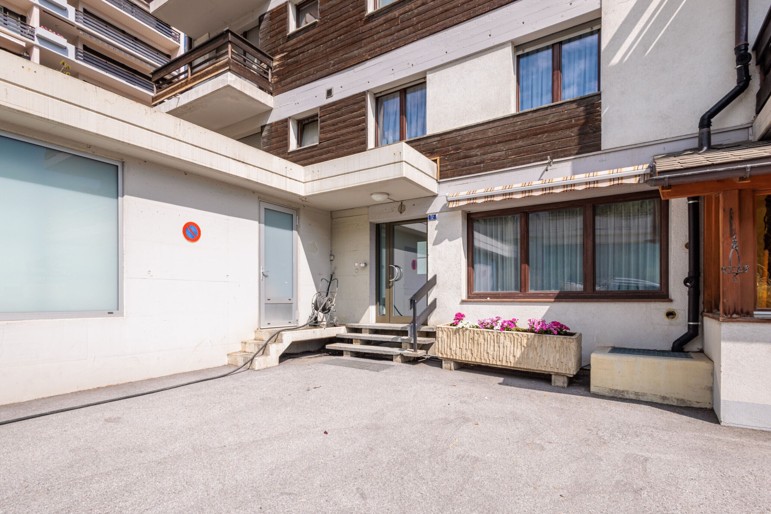 A multi-story residential building with a central staircase, a small porch area with flowers, and a visible door.