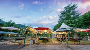 Un espacio al aire libre con mesas y sombrillas, rodeado de vegetación y colinas.