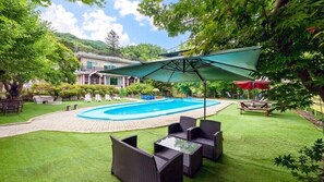 Piscina com um terraço ao redor, incluindo mobiliário de vime e uma área de estar coberta.