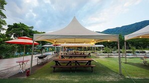 Un área de comedor al aire libre con mesas de picnic y una gran carpa.