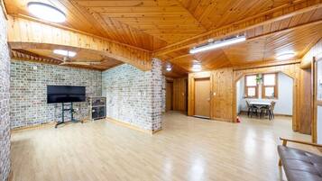 A spacious room with a brick wall, wooden ceiling, a flat-screen TV, a table with chairs, and a bench.