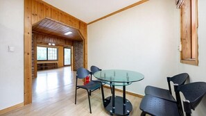 Um quarto com uma mesa de vidro redonda, quatro cadeiras pretas, paredes de madeira e um extintor de incêndio à vista.
