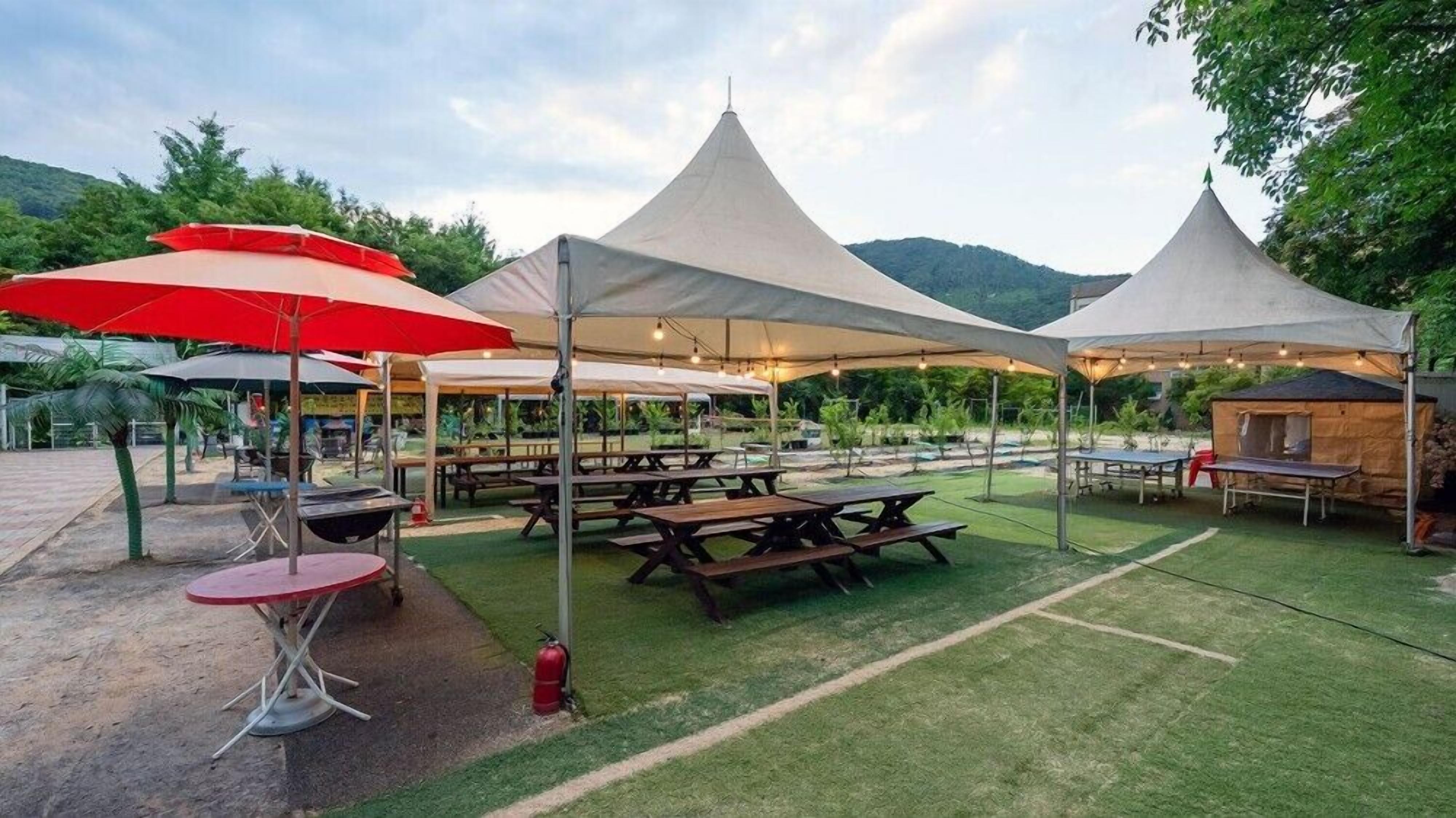 A campsite with multiple picnic tables and tents, surrounded by greenery and hills.