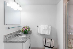 Une salle de bain avec un comptoir en granit, un lavabo, un miroir et une douche.