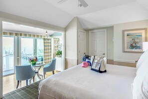 Une chambre d’hôtel avec un grand lit, un balcon avec une table et des chaises, et un tableau accroché au mur.