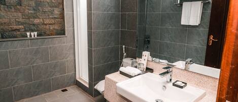 A modern bathroom with a stone wall, a large sink, and a glass shower enclosure.