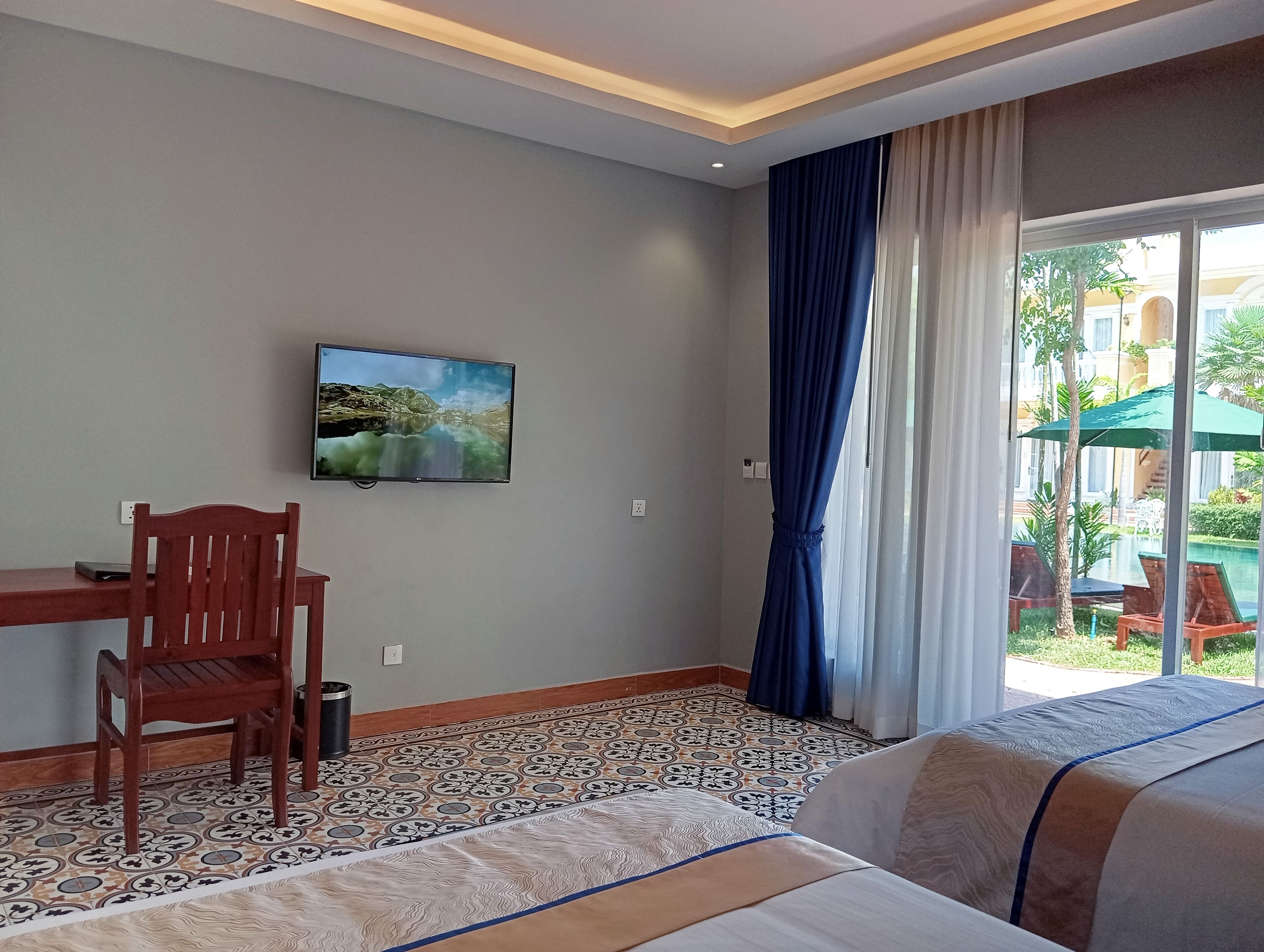 Habitación de hotel con cama, escritorio y silla, televisión en la pared y ventana con cortinas.