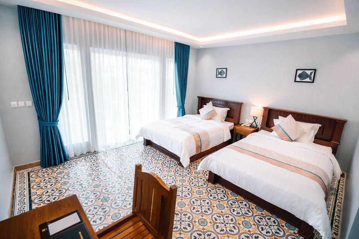 A hotel room with two beds, a wooden chair, a desk, and a patterned floor.