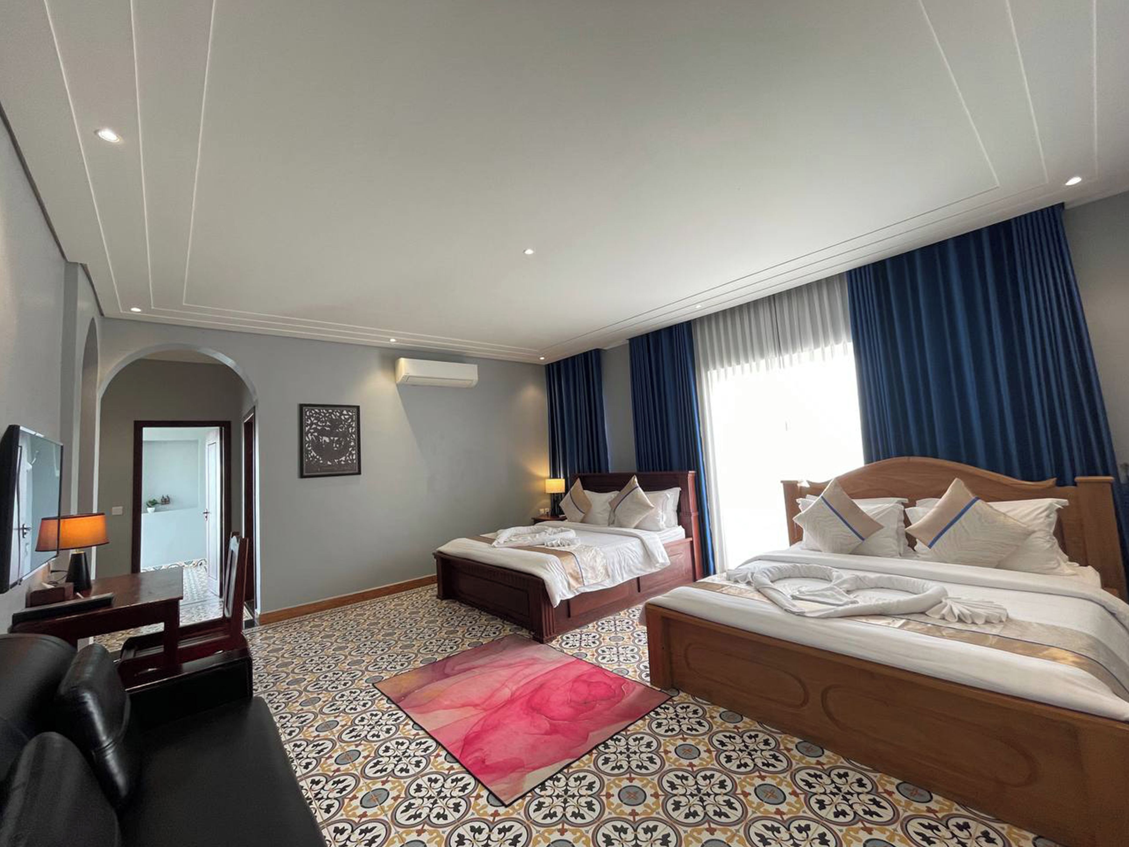 A hotel room with two beds, a desk, a chair, a TV, and a patterned floor.
