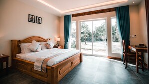 A bedroom with a wooden bed, a desk, and a view through a glass door. - Sokchea Kampot Hotel (Kampot)