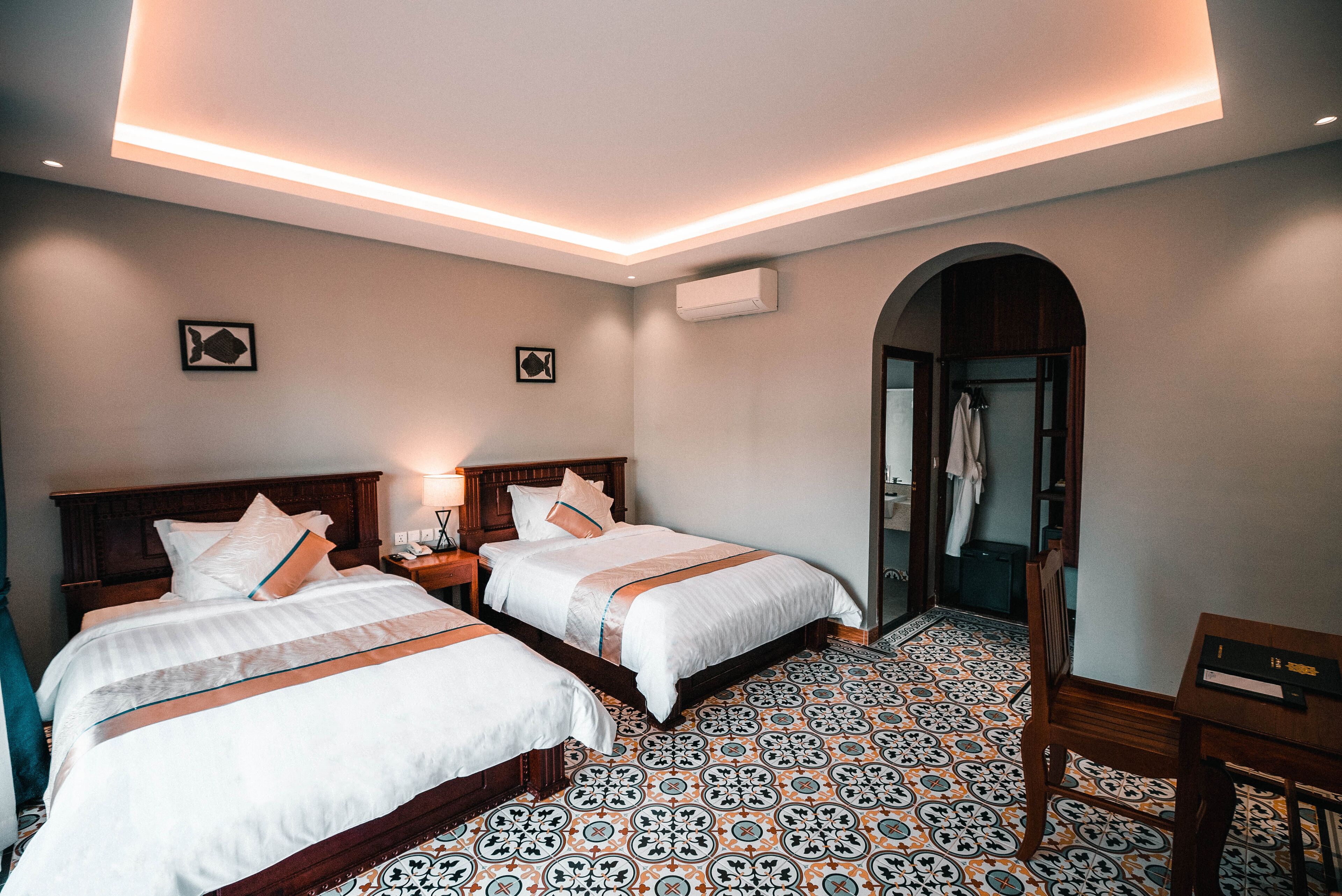 A hotel room with two beds, a tiled floor, a wooden headboard, a nightstand, and a mirror.