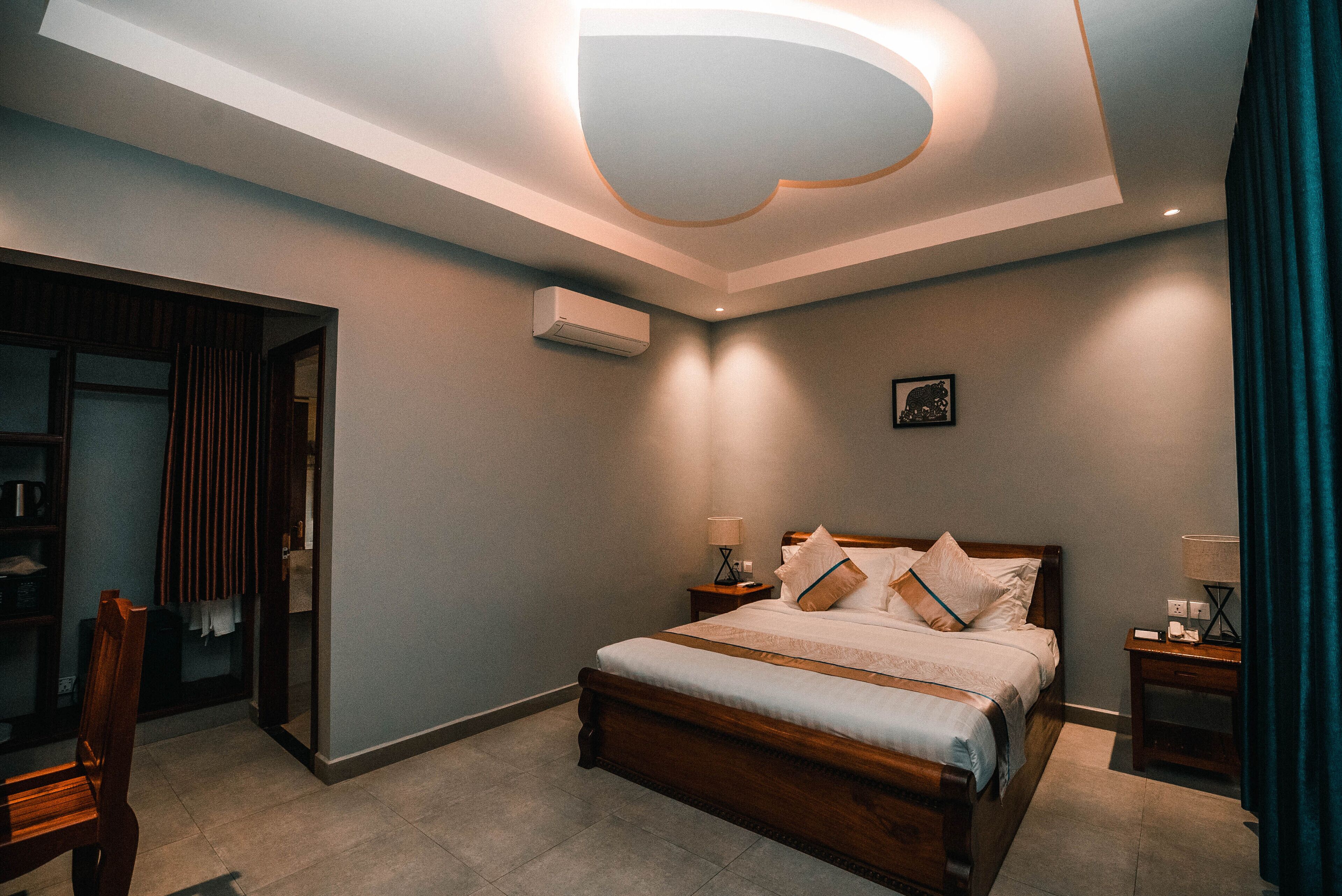A modern bedroom with a wooden bed, bedside tables, a wall-mounted air conditioner, and a ceiling light fixture.