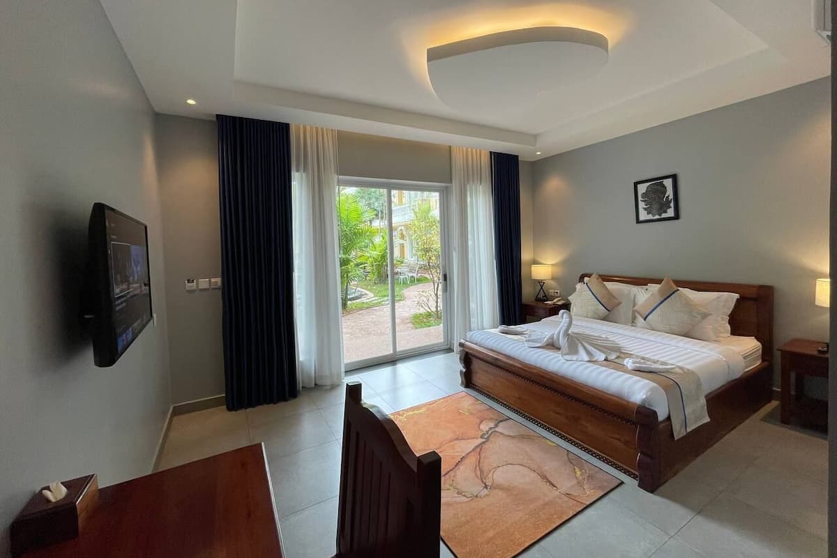A hotel room with a bed, a desk, a chair, a TV, and a view of the outdoors.