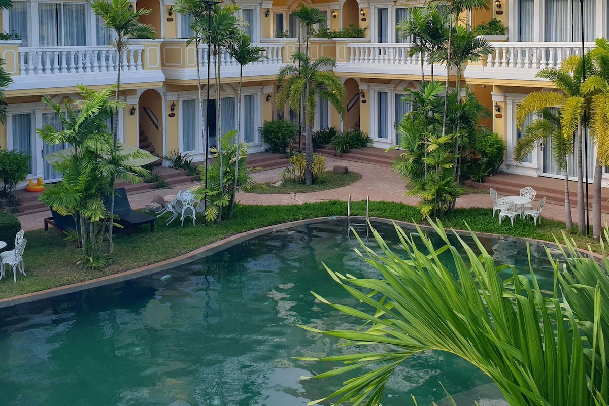 A hotel with a pool, outdoor seating, and lush greenery.