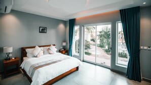 A modern hotel room with a large bed, a nightstand, a lamp, and a view of the outdoors through a sliding glass door. - Sokchea Kampot Hotel (Kampot)