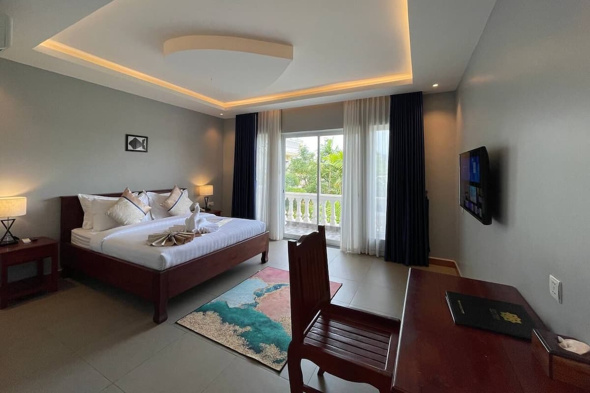 A hotel room with a bed, a desk, a chair, a TV, and a balcony with curtains.