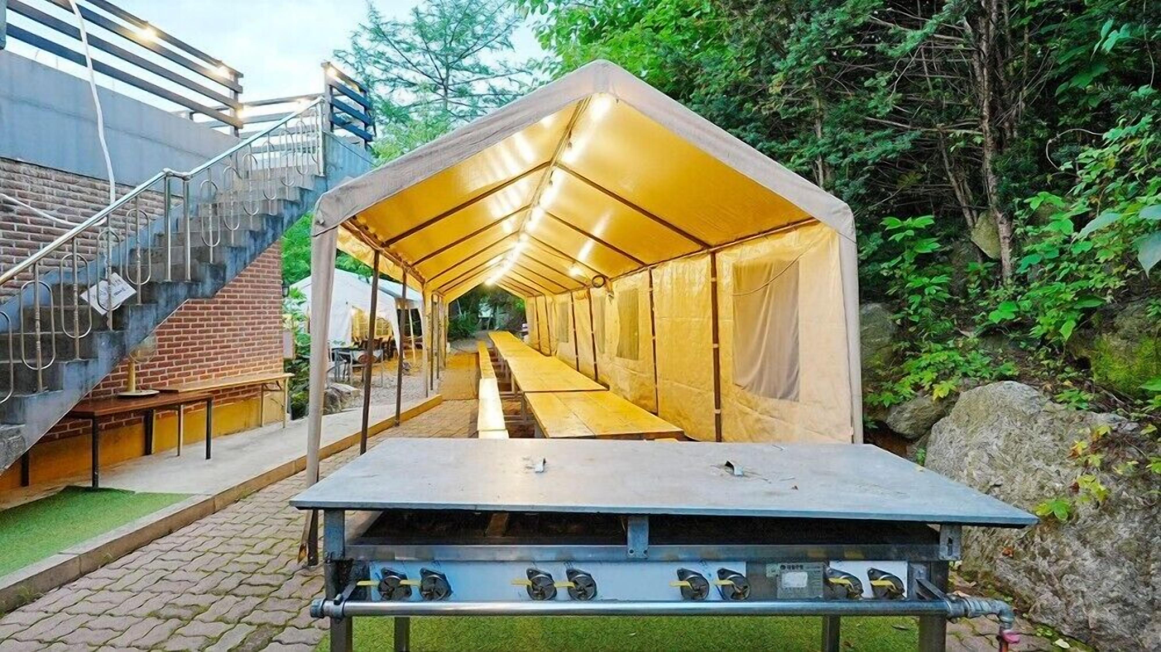 Un espacio al aire libre con carpas, una parrilla, una mesa con parrilla y una escalera que sube a un nivel superior.