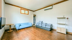 A room with a blue sofa, a small round table, a stack of folded blankets, a wardrobe, and a mounted air conditioner.