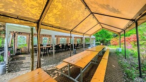 A covered outdoor seating area with tables and chairs, surrounded by a garden with trees and shrubs. - Heaven Valley B (Namyangju)