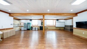 A spacious room with a wooden floor, a whiteboard, a television, and a kitchenette area.